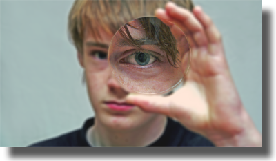 En pojke kikar genom ett förstoringsglas så att ena ögat blir större.